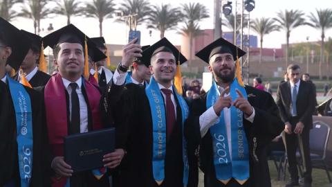 Males are standing and smiling. They are wearing caps and gowns