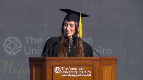 A woman is standing ata podium wearing a cap and gown