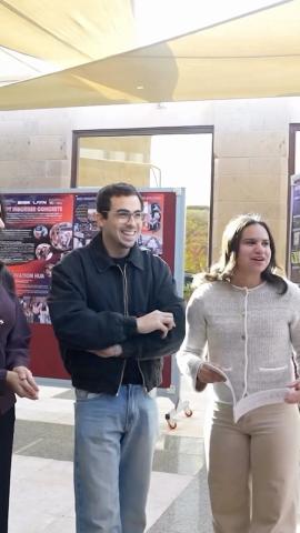 A male and a female are standing, looking at someone and smiling