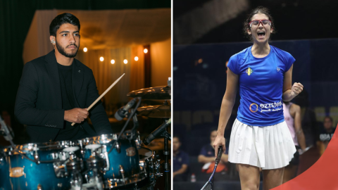 A male is playing the drums and a female is holding a squash racket and cheering for herself