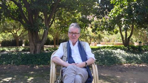 A man is sitting on a chair and smiling. He is wearing glasses