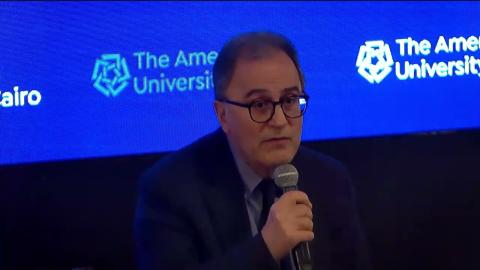 A man is talking into a microphone, he is wearing glasses