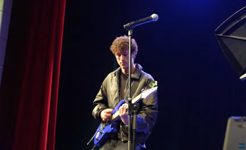 A male is playing on an electric guitar. There is a microphone in front of him