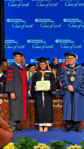 Two males and a females are standing and smiling. They are wearing graduation caps and gowns. The female is holding a graduation certificate