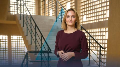 A female is standing and smiling. There are stairs behind her