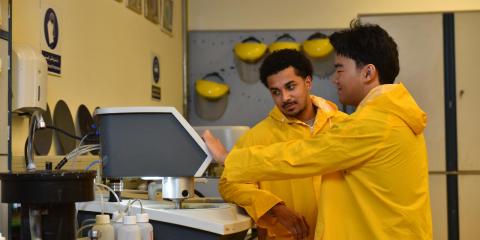 Two young males standing in a lab. They are wearing yellow coats