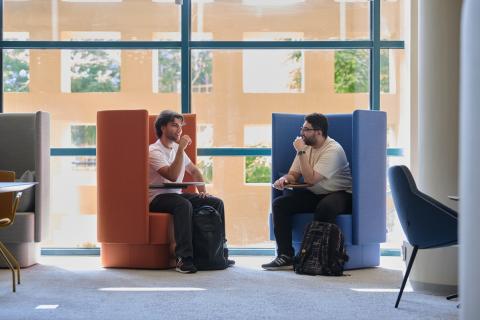 Two males are talking and sitting on round colored chairs 
