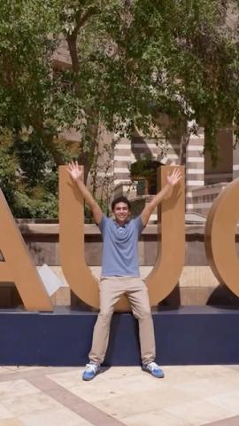 A male is smiling and standing in front of the big letters AUC