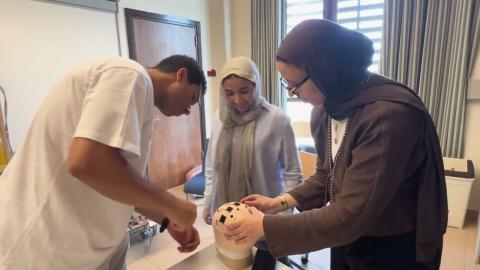 A male and two females are in a lab. They are holding a helmet