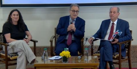 Two men and a woman are sitting at a table. The male in the middle is talking into a microphone