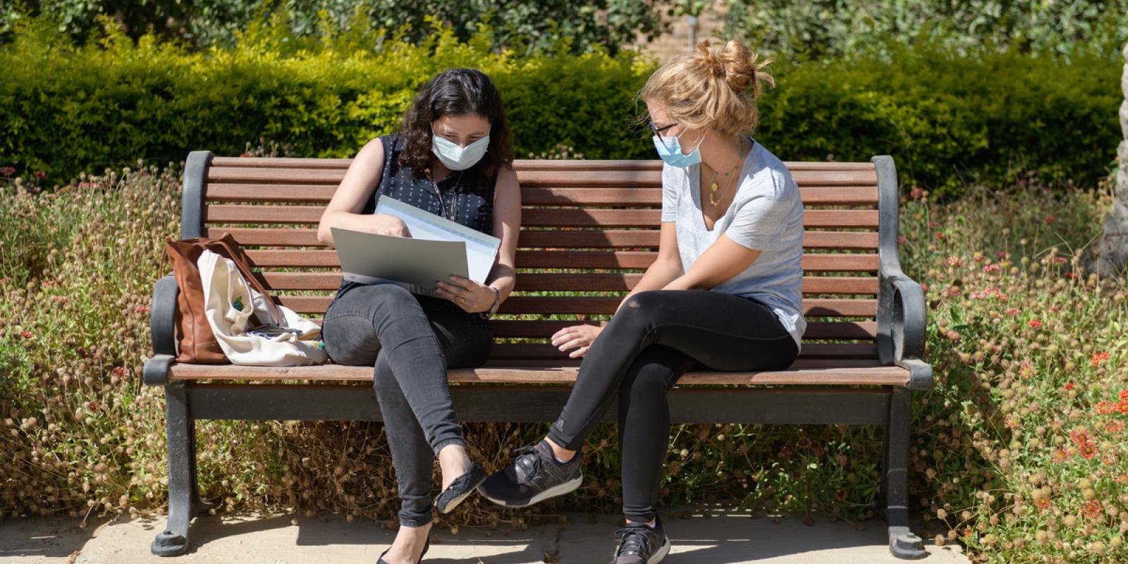 Two masked girls studying on a bench