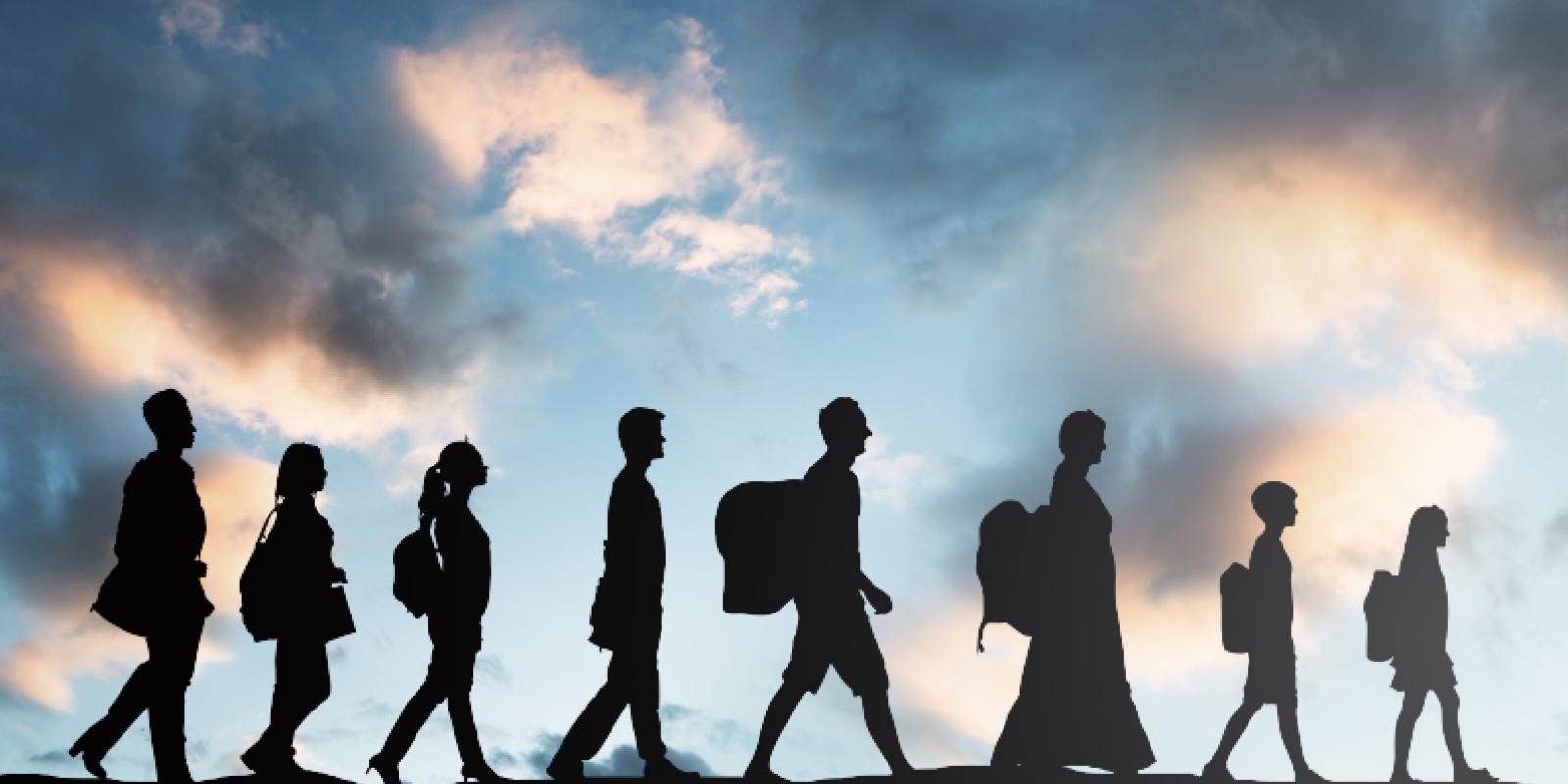 Silhouette of people walking in a line with the sky illuminated behind them