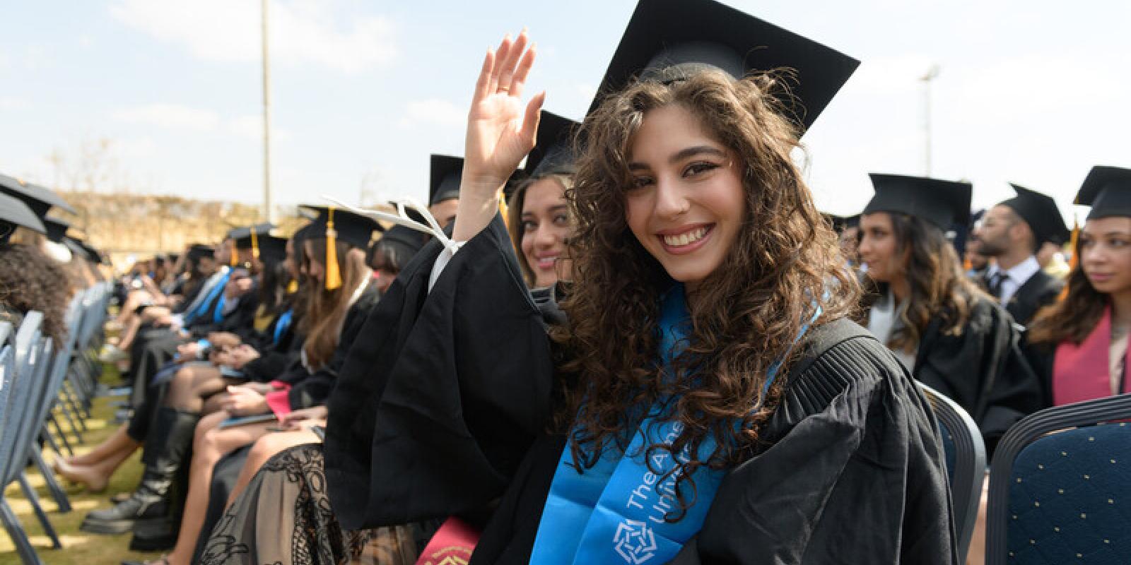 Students in cap in gown sit at commencement