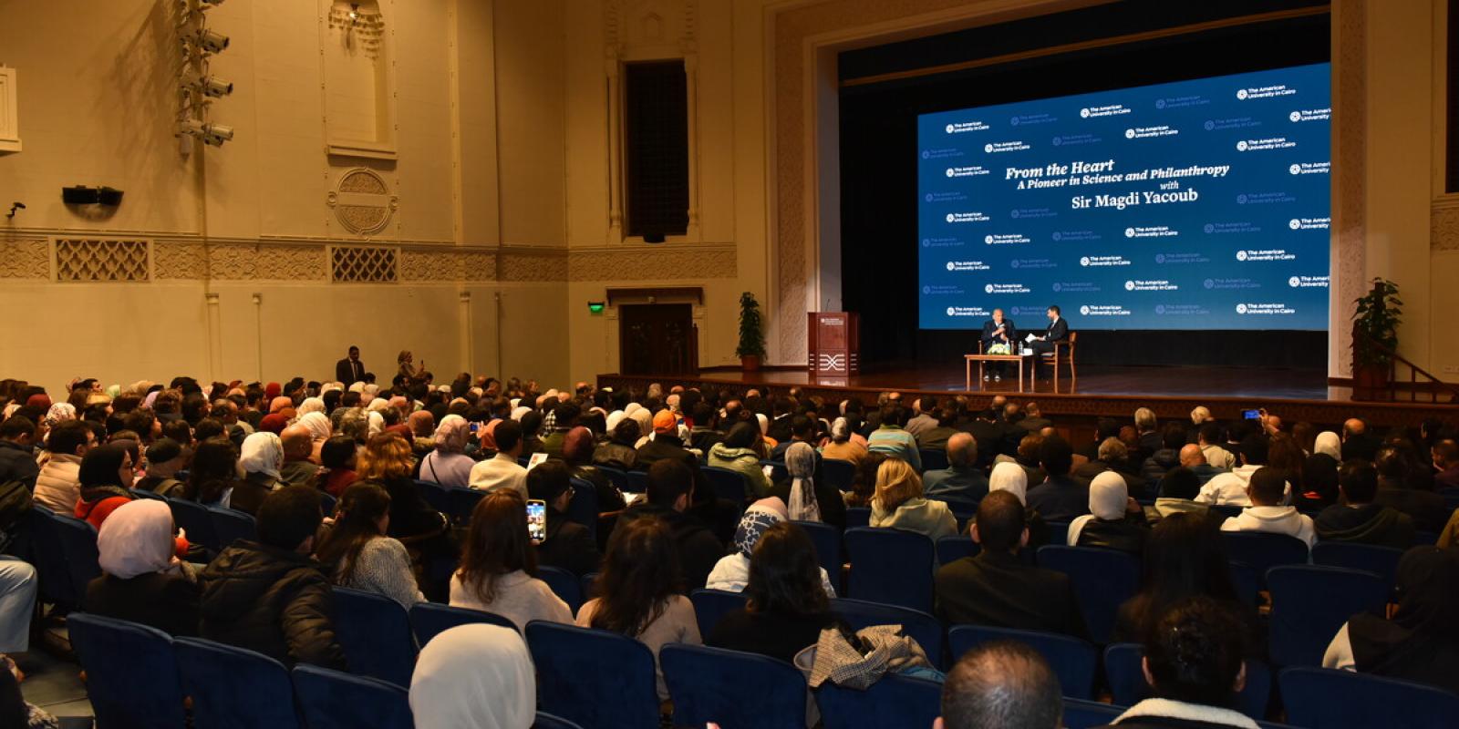 People sitting in a hall listening to people on stage