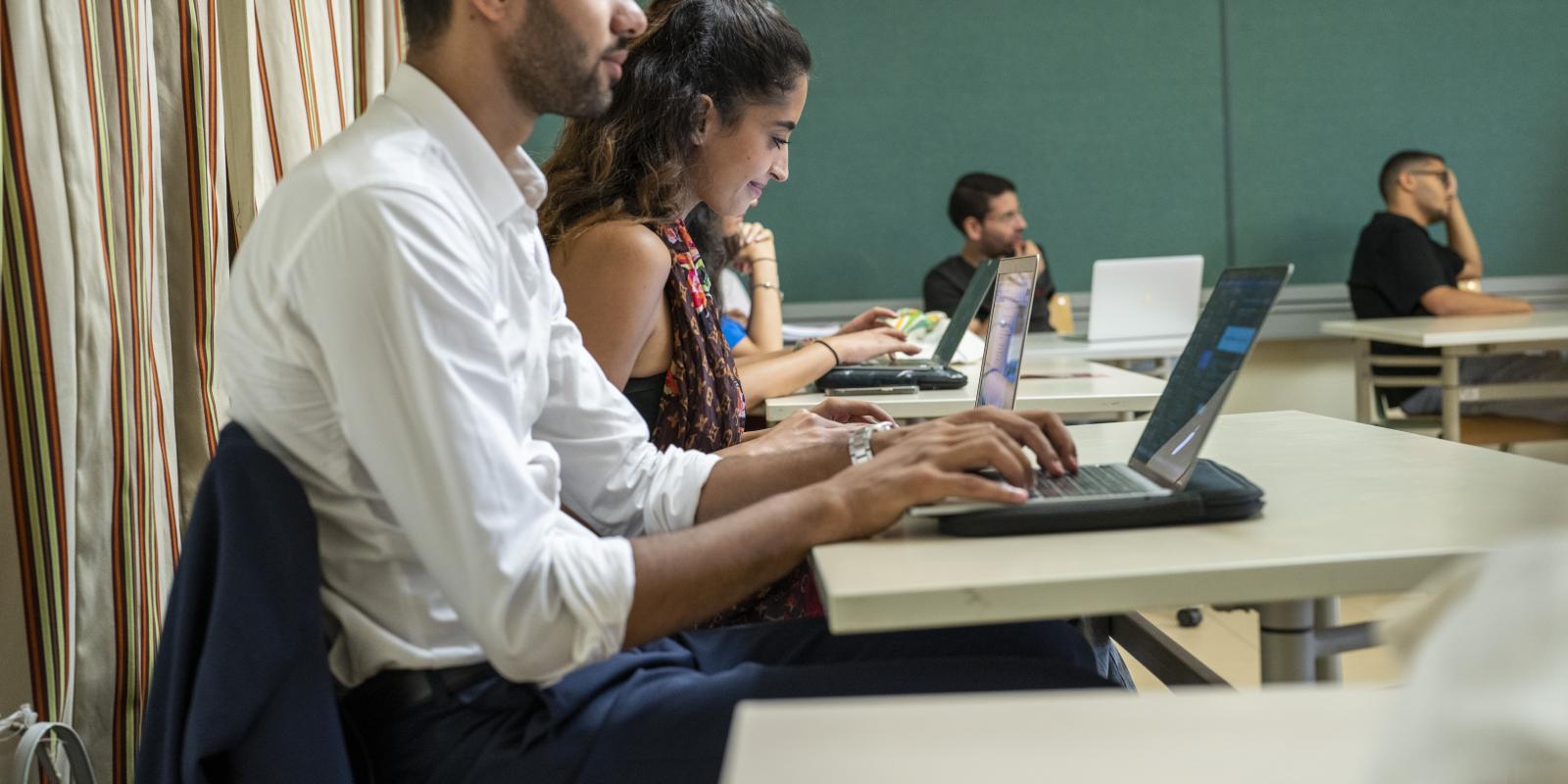 students taking notes on laptops in classroom lecture