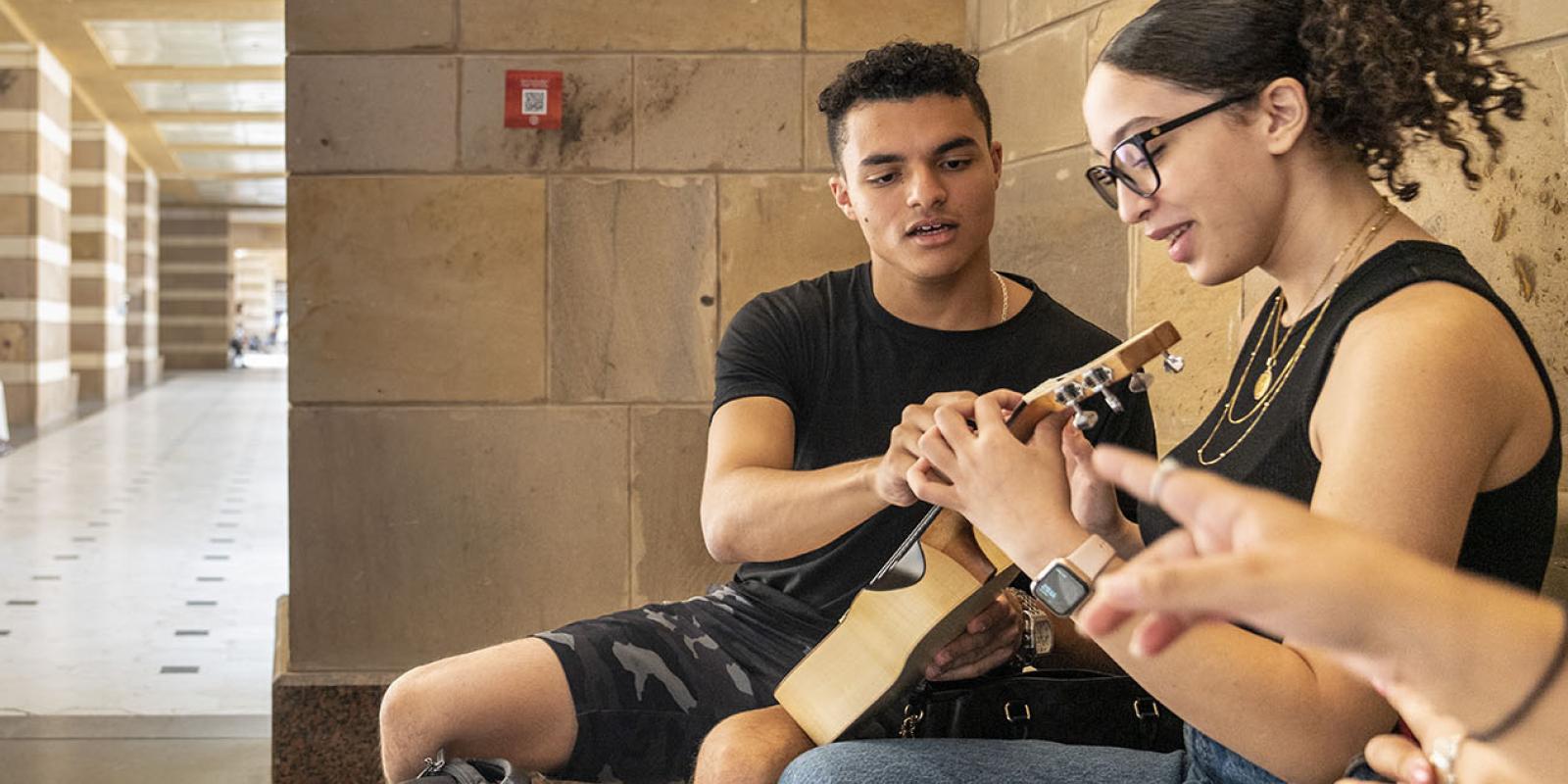 A girl and boy on AUC campus playing the guitar