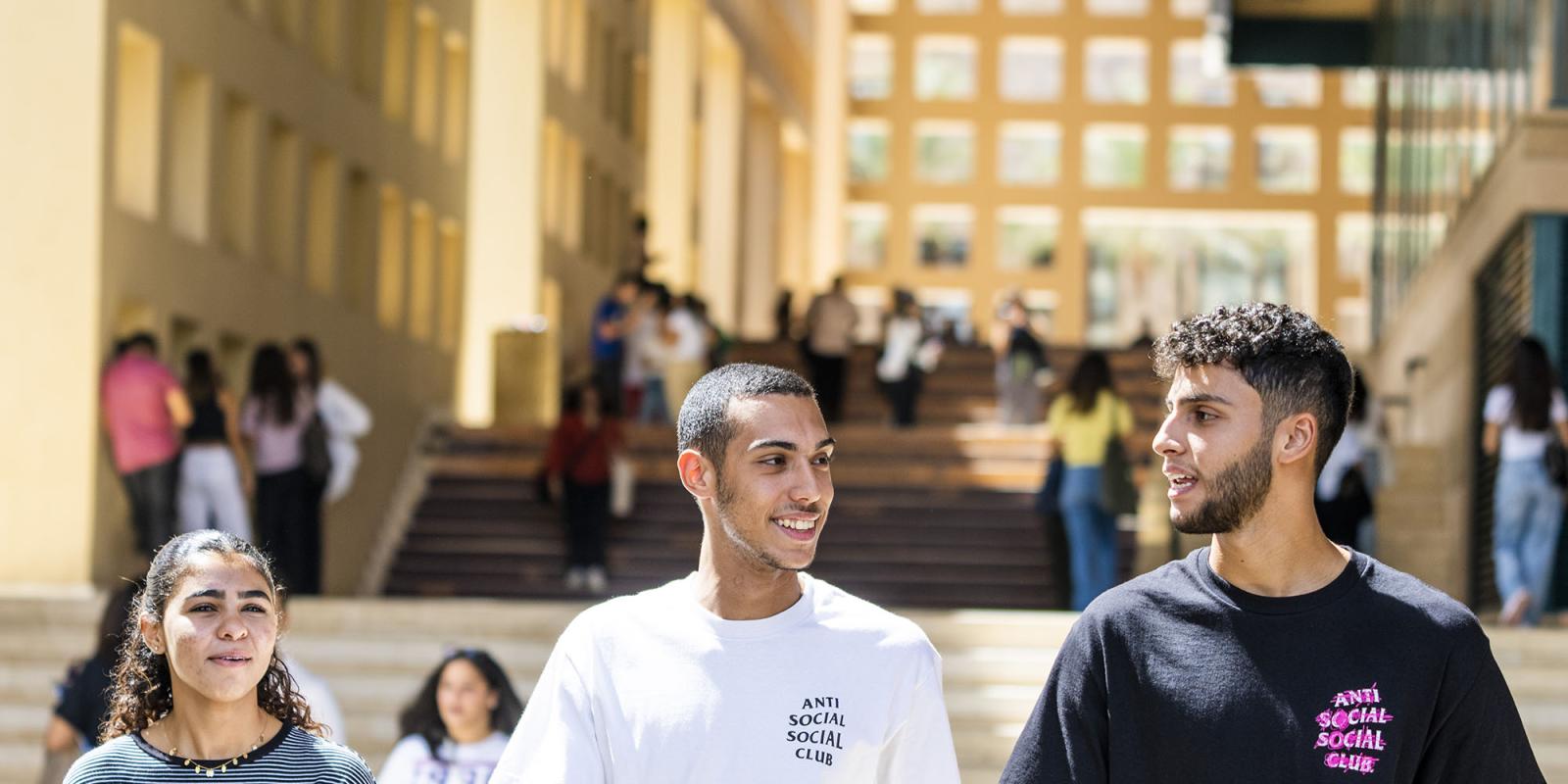 Two boys and a girl walking on campus by building