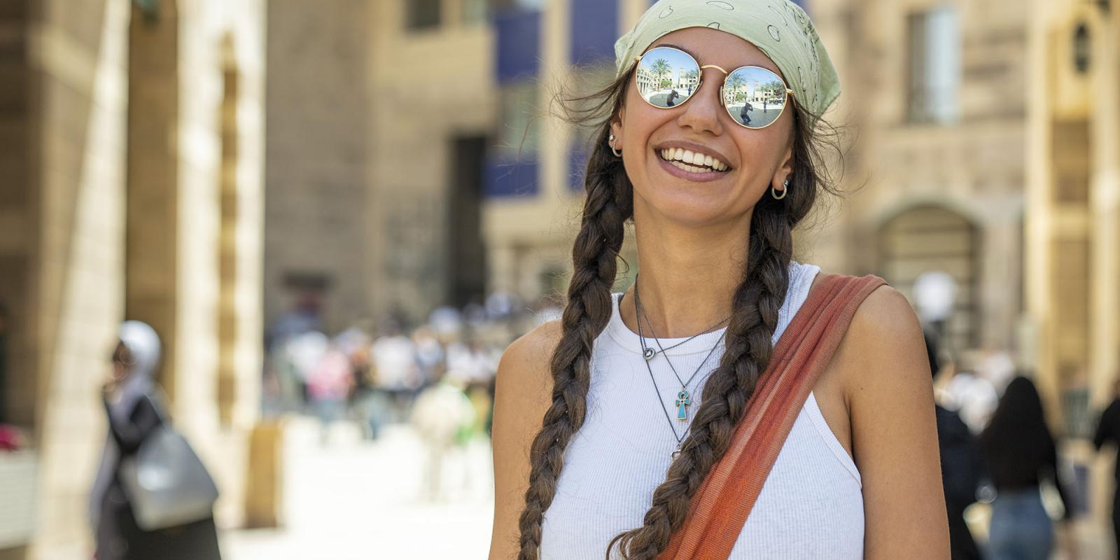 Girl wearing sunglasses and a head bandana smiling on campus