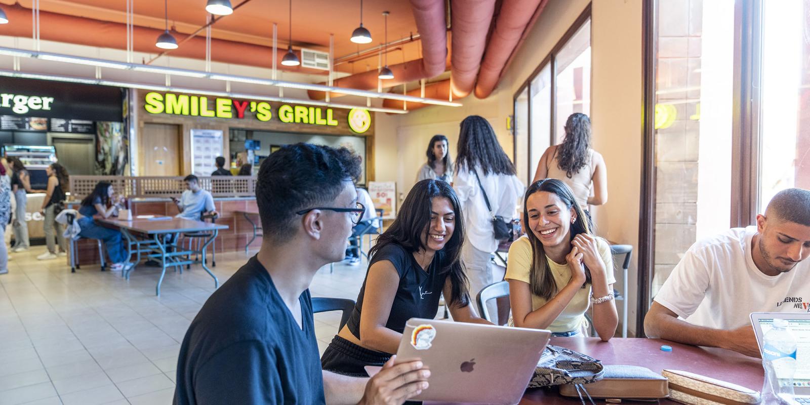 Group of students in food court with a boy holding his laptop