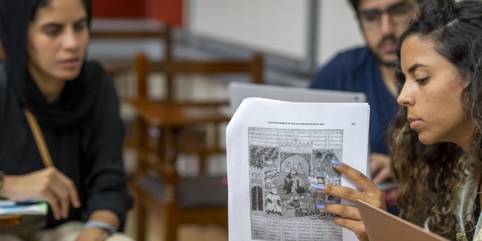 A girl holding a paper explaing to other students in a classroom
