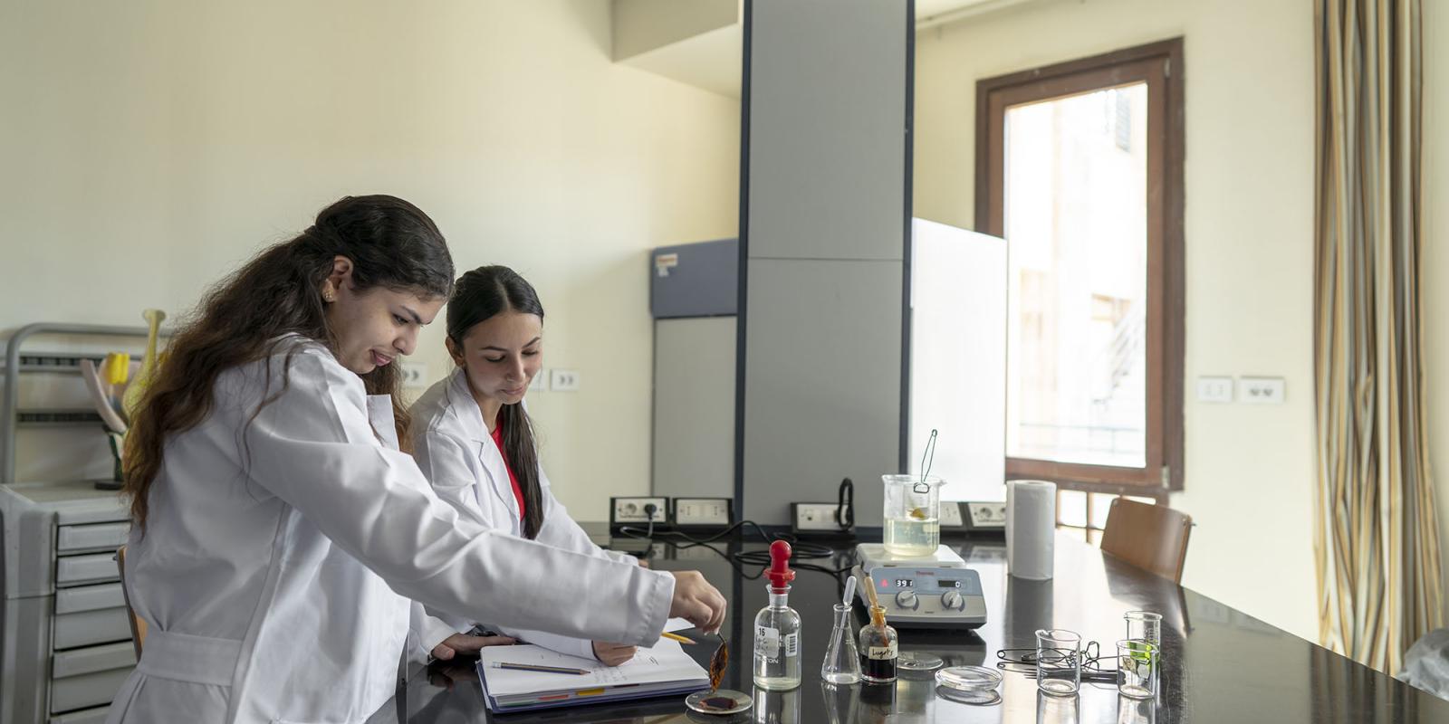 two girls wearing white lab coat conducting an experiment in a lab