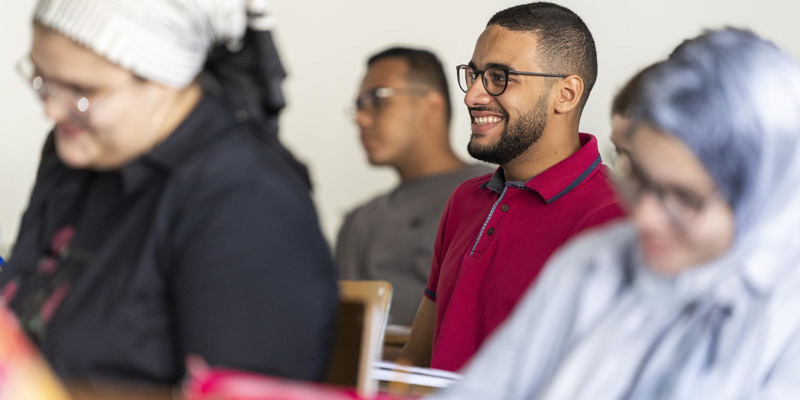 A boy sitting in class with glasses smiling