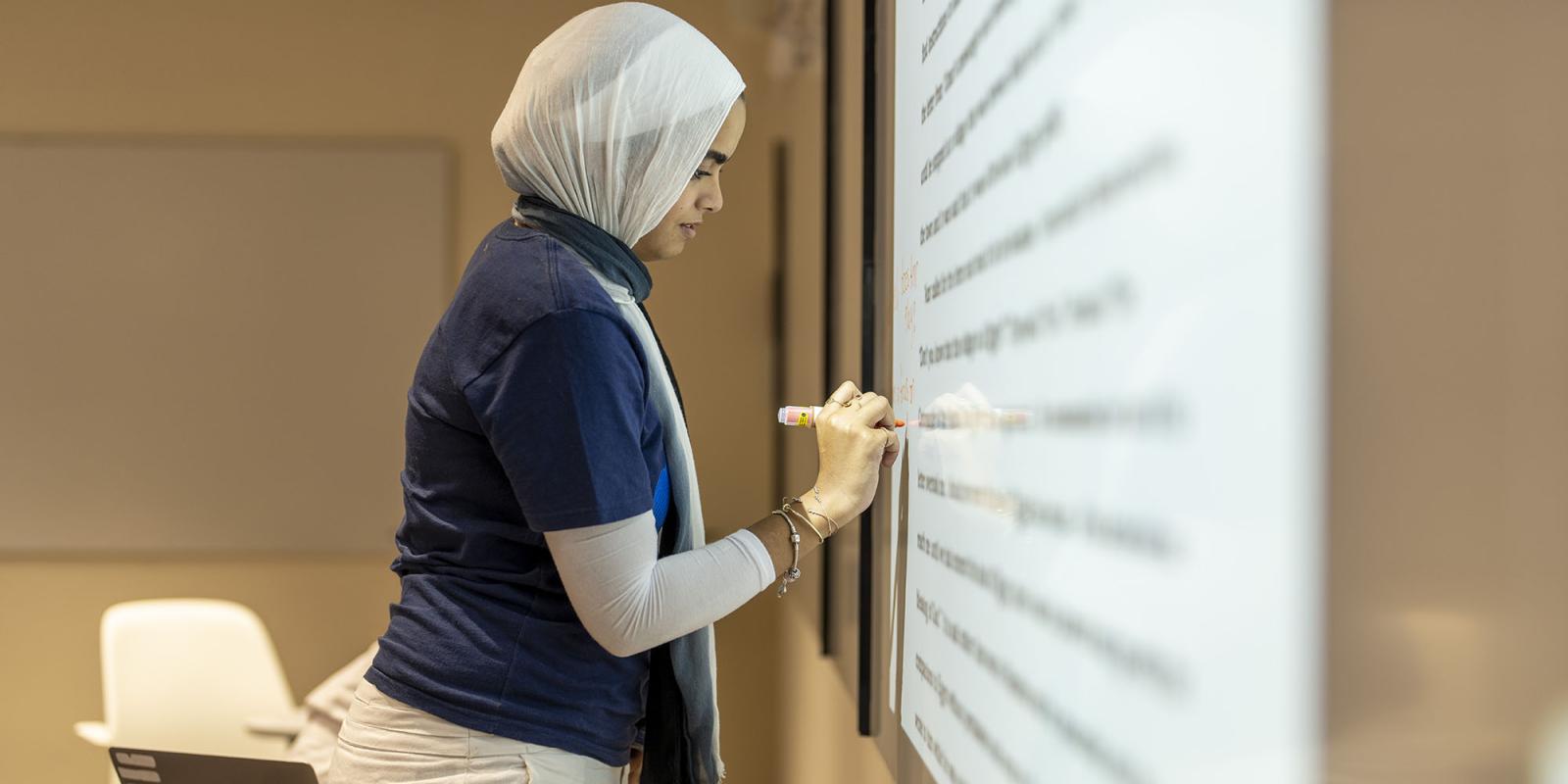 Female student writing on a screen in class