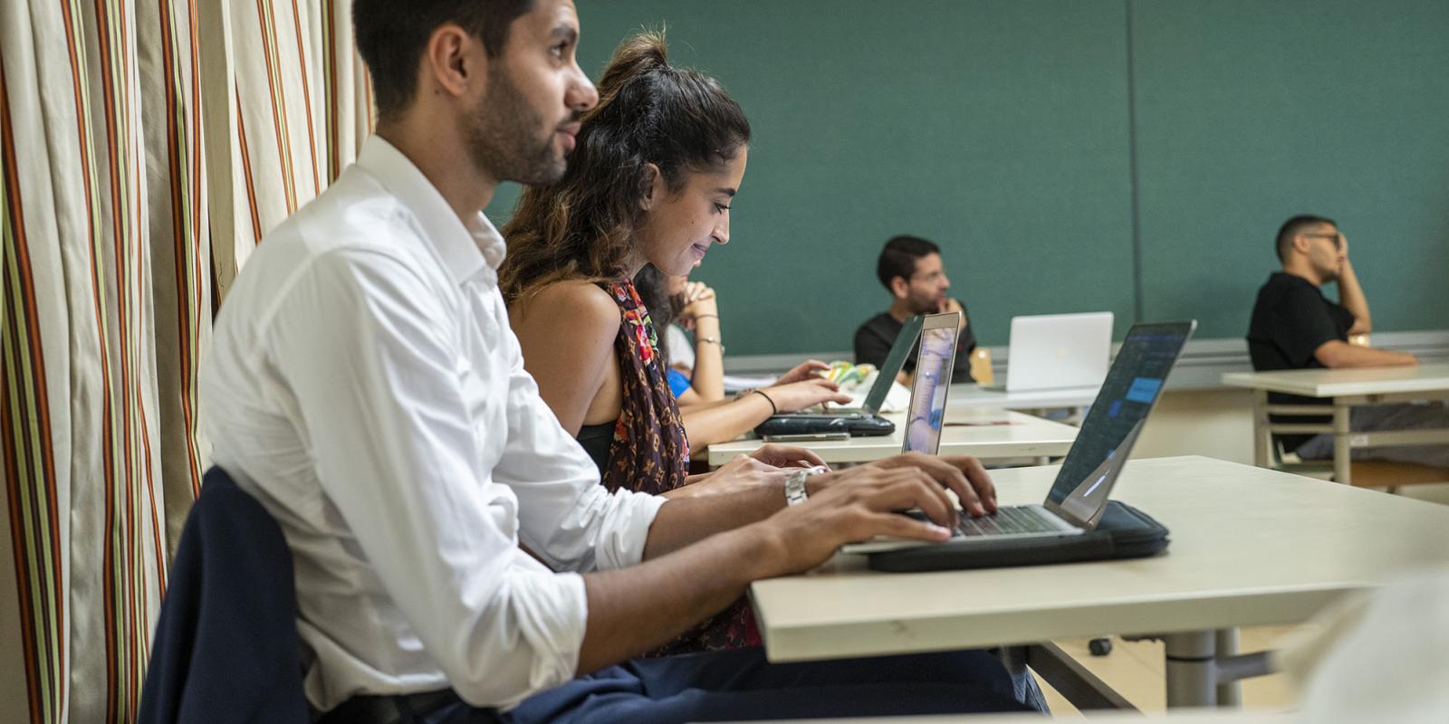 Students sitting in class and typing on their laptops