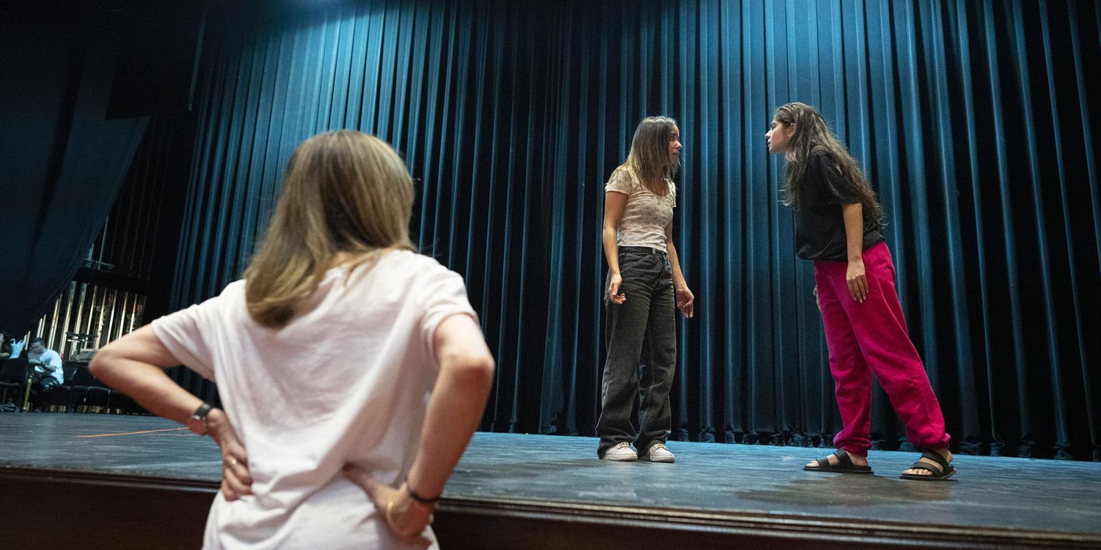 Instructor watching two female students acting on stage