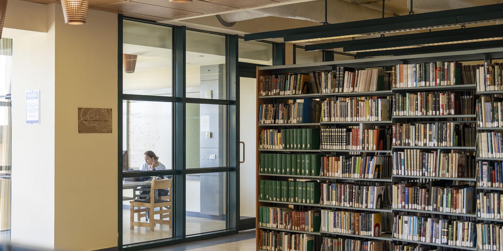 Female student studying in a glass room in the library next to book shelves