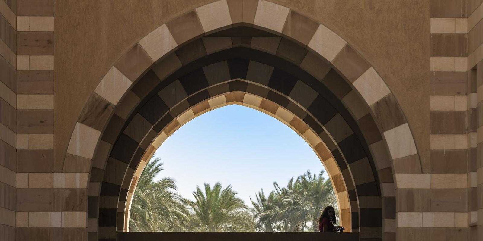 Student standing under an arch with palm trees in the background