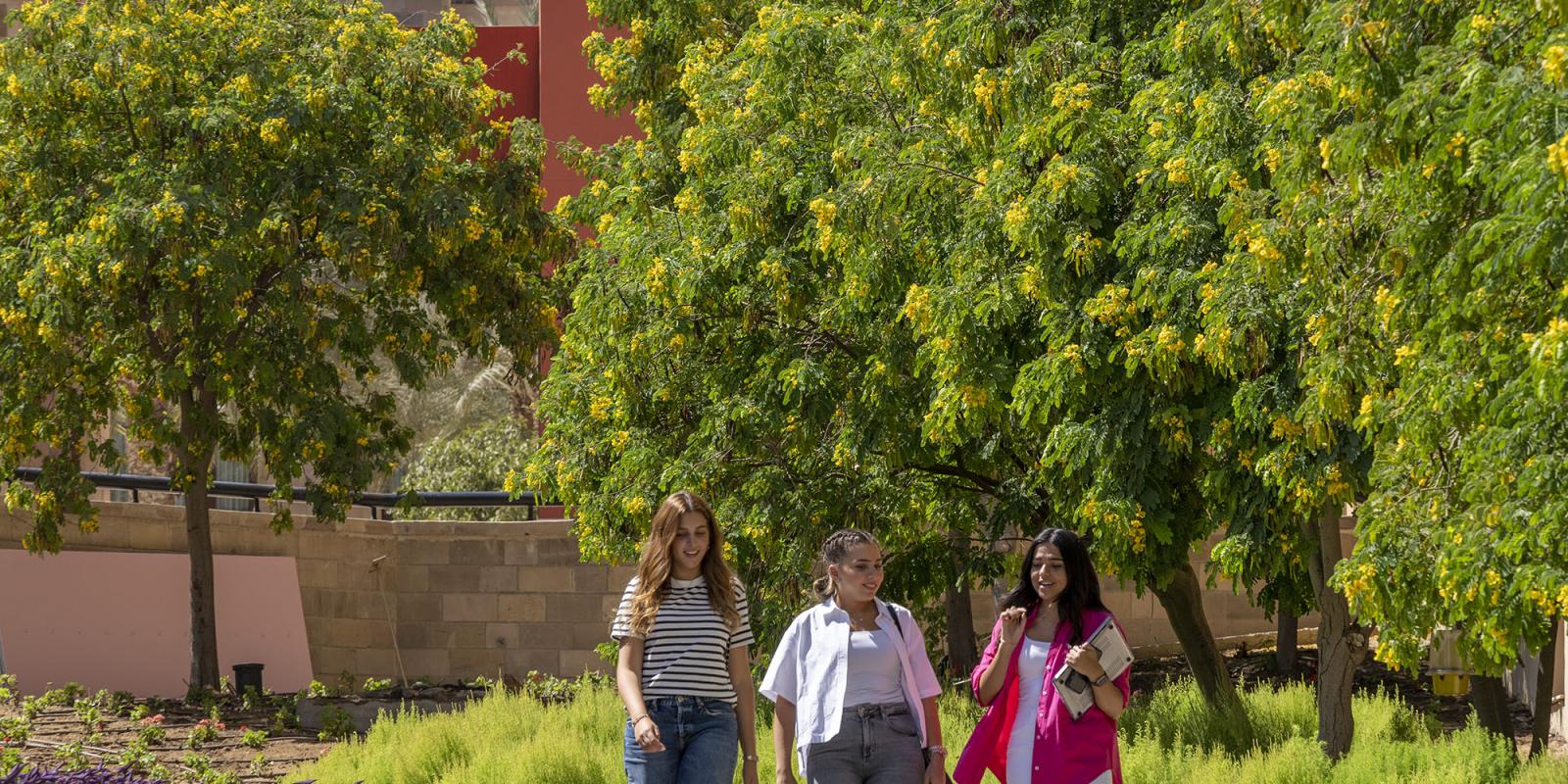 Three female students walking and talking in the garden.