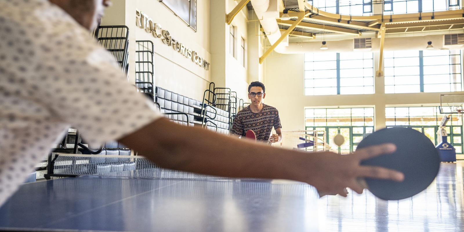 Two male students holding rackets in their hands and playing table tennis in Artoc Sports Court.