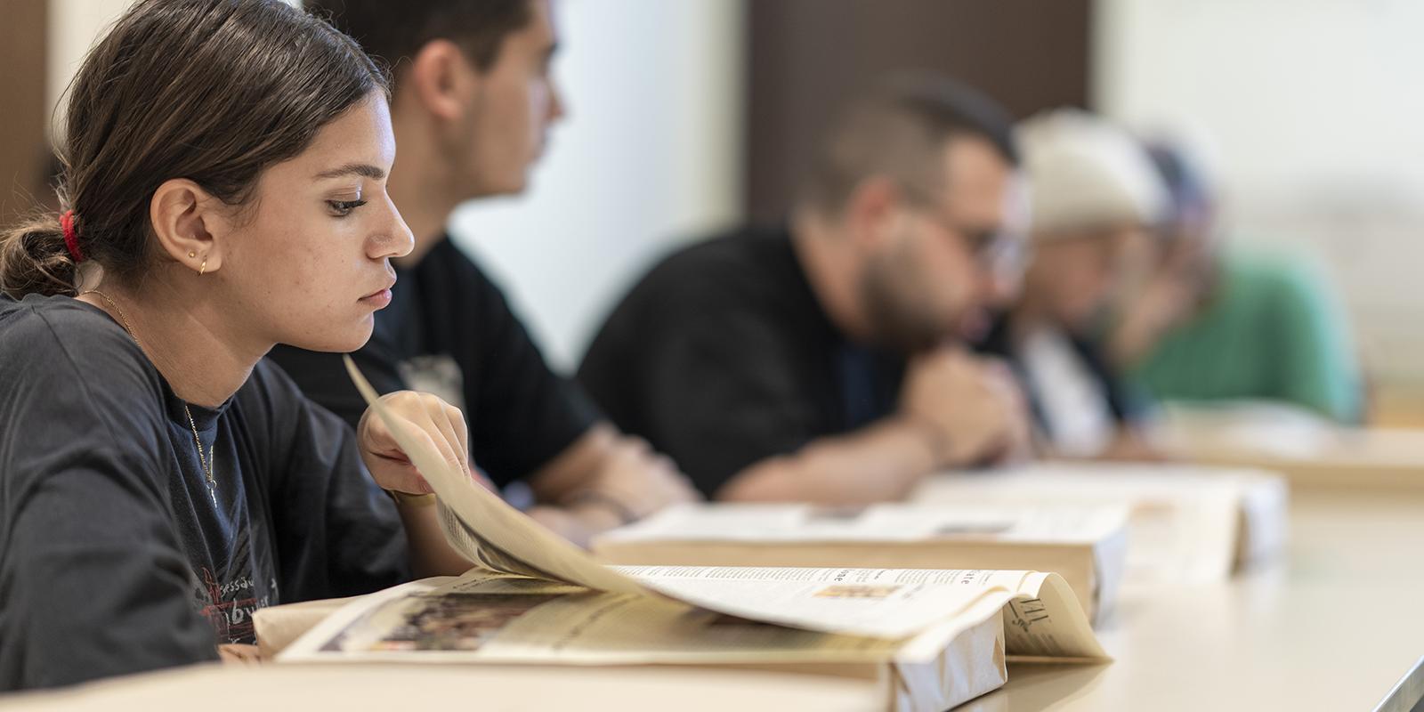 Girl sitting in a classroom flipping page of book infront of her