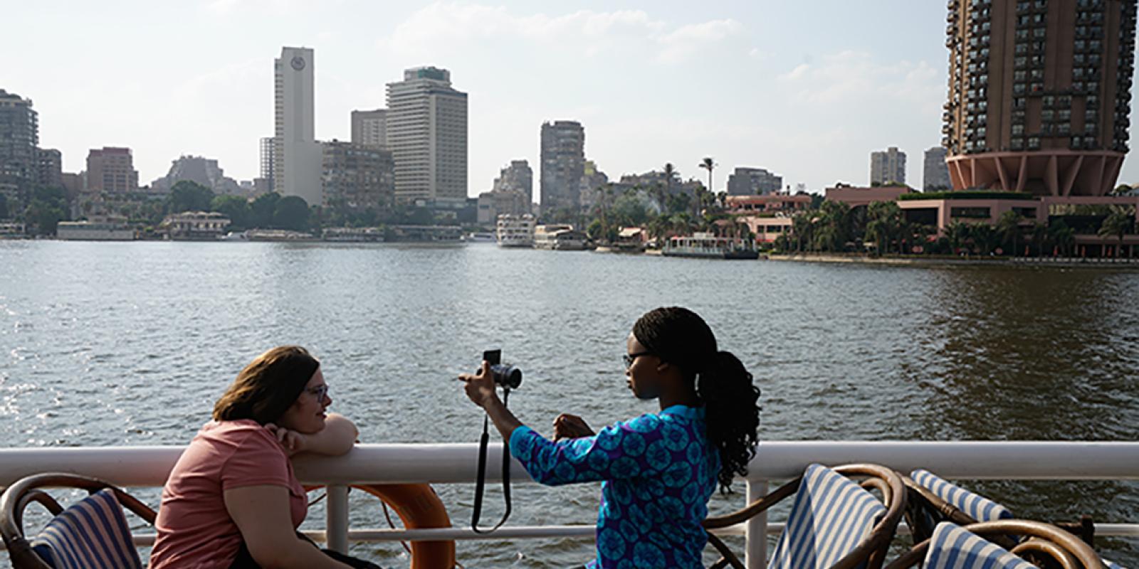 A girl taking picture of another girl using a camera by the nile