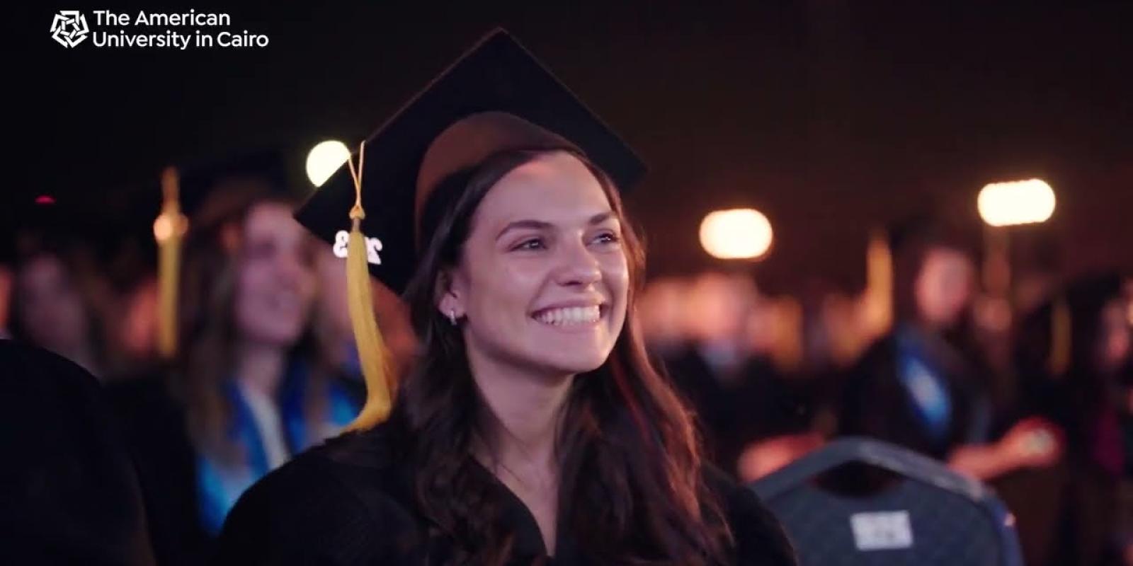 A female is smiling and wearing her cap and gown during graduation