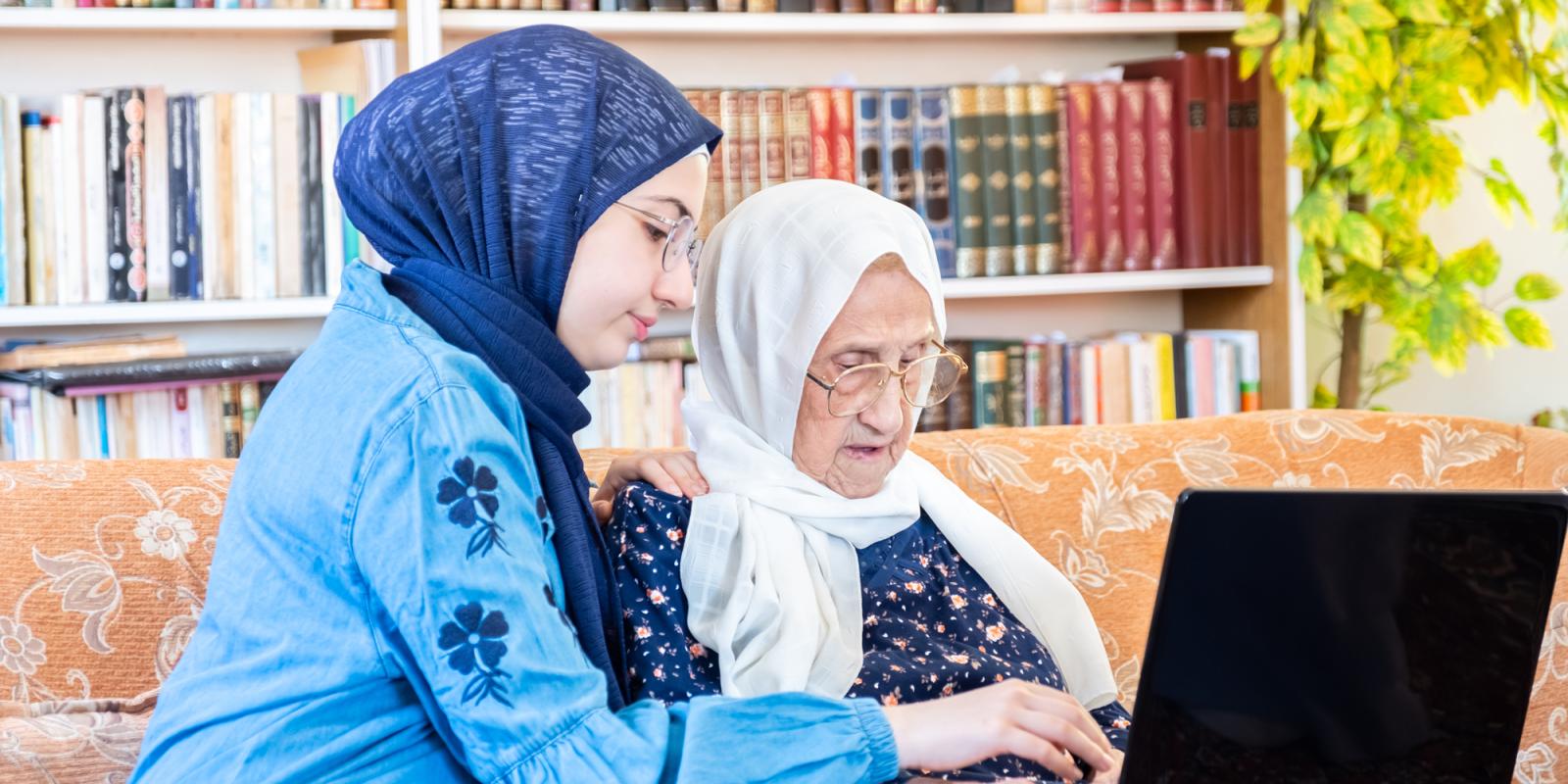 lady sitting with an elderly lady working together on a laptop