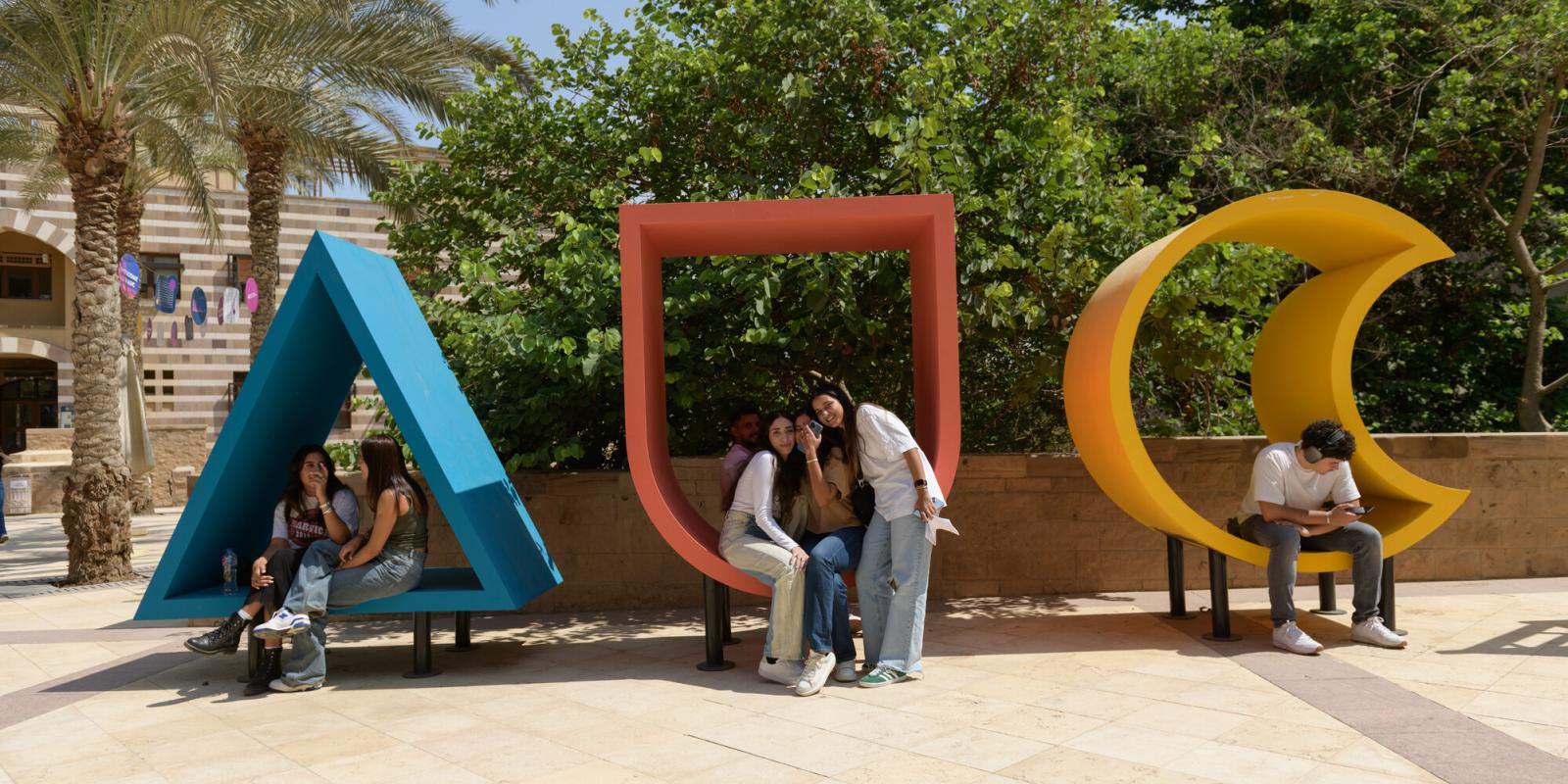 Girls sitting in a big letter figurine on campus