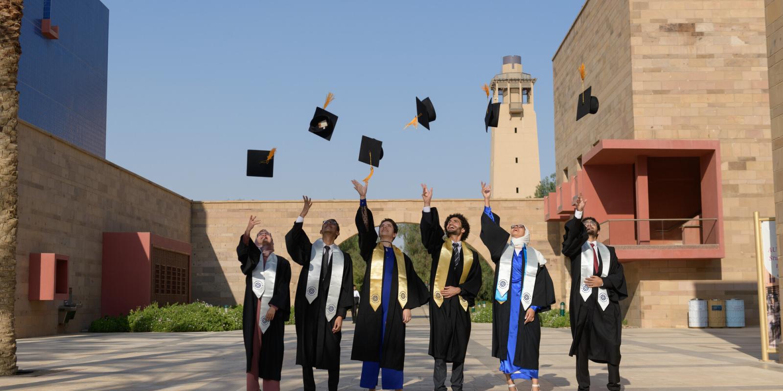 A group of students wearing gowns and throwing their cap in the air on AUC campus