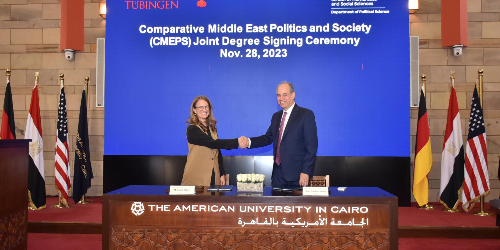 A man and a woman shake hands in front of a blue background