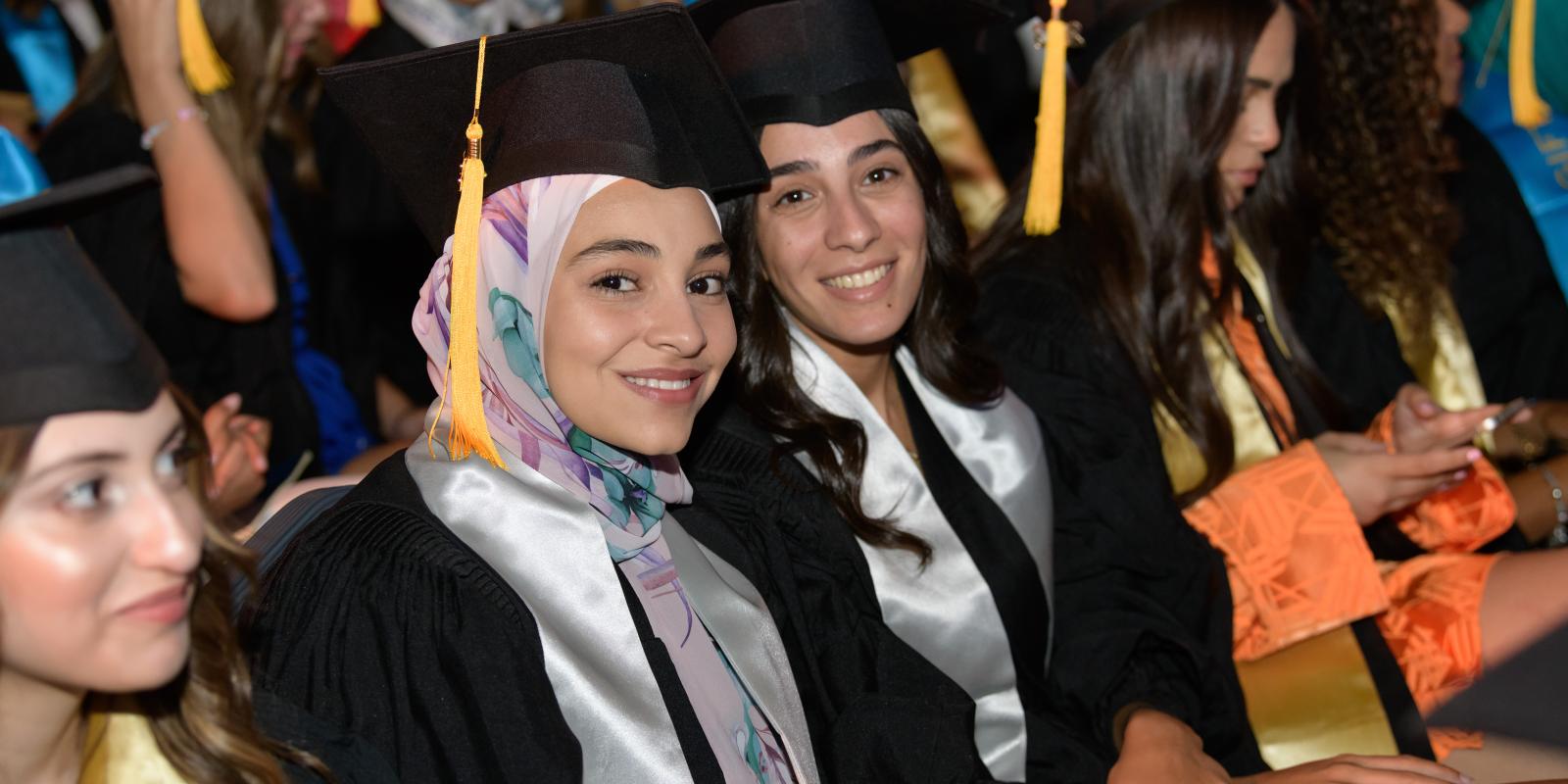 Students in caps and gowns smile in a crowded room