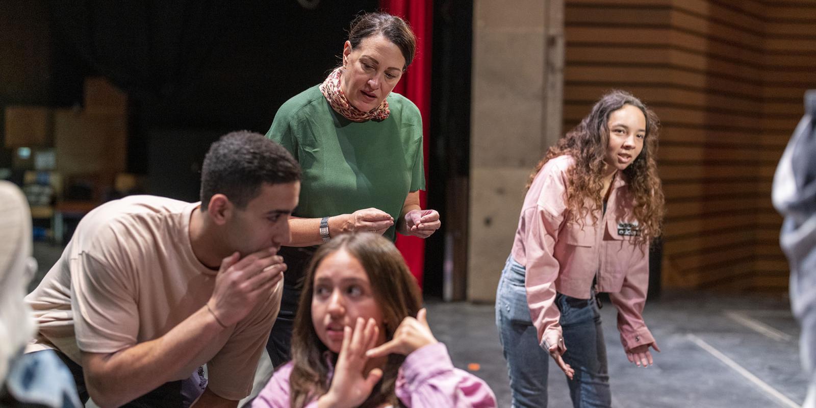 A woman in a green shirt works with students onstage