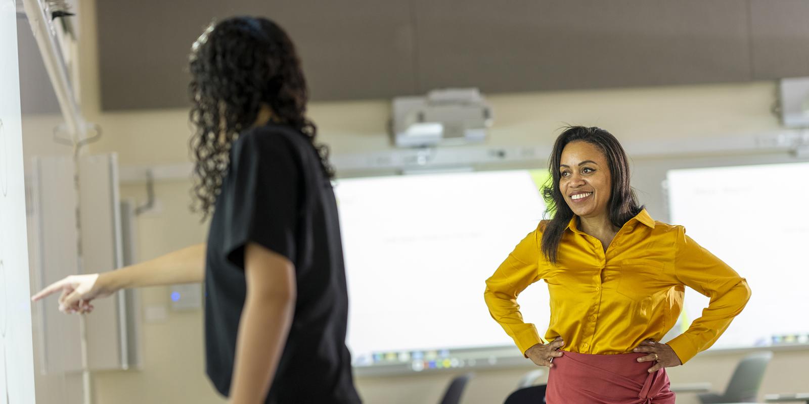 Woman in a yellow shirt works with a student in front of a whiteboard