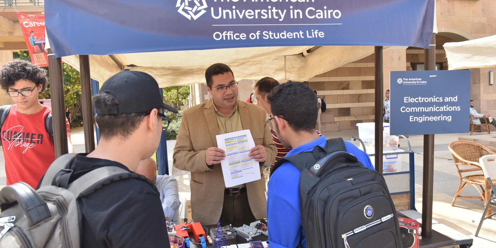 2 new students talking to professor about courses in Explore the Disciplines Fair at AUC