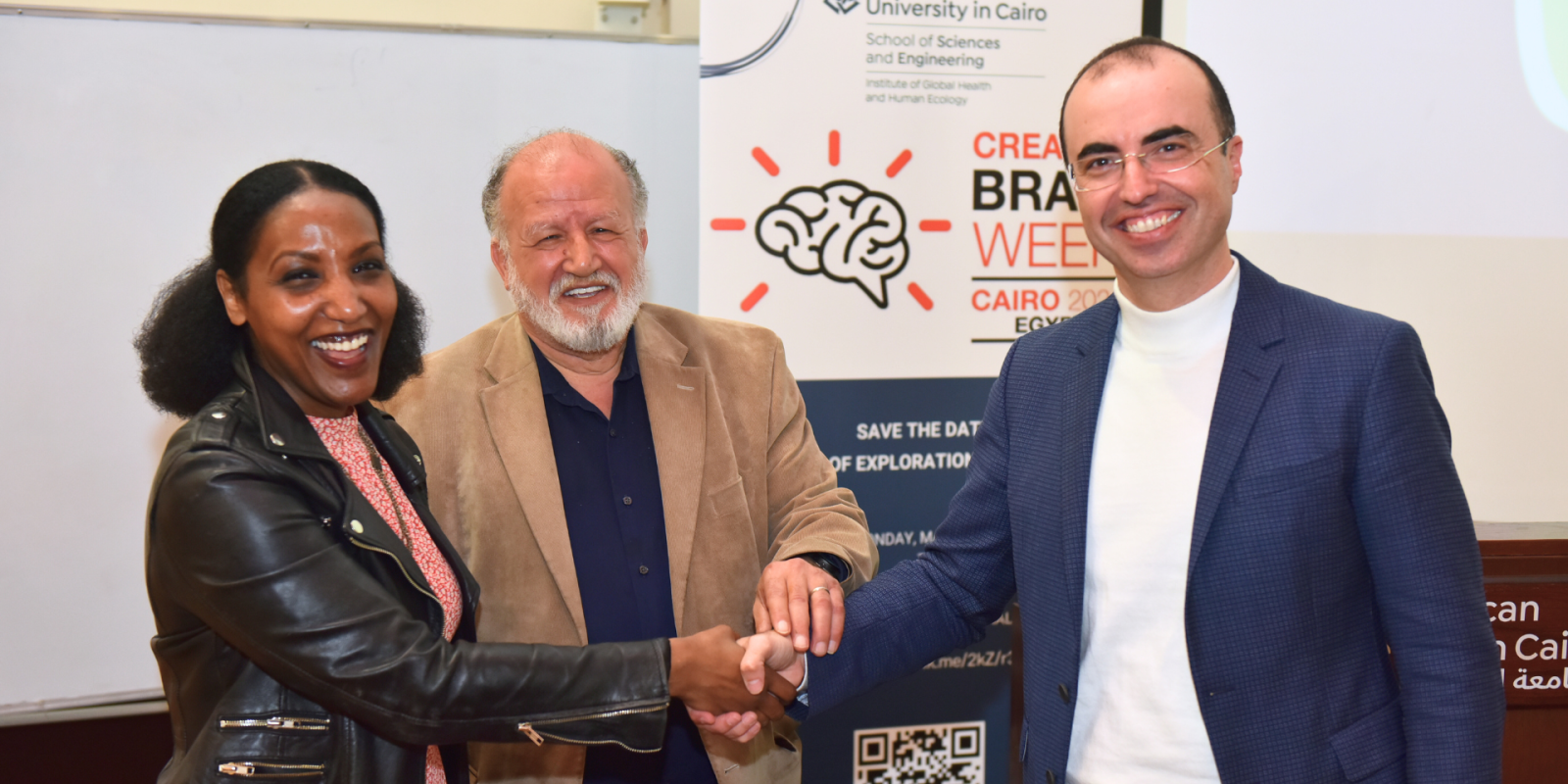 Two men and a woman shake hands in front of a background from Brain Week 2024