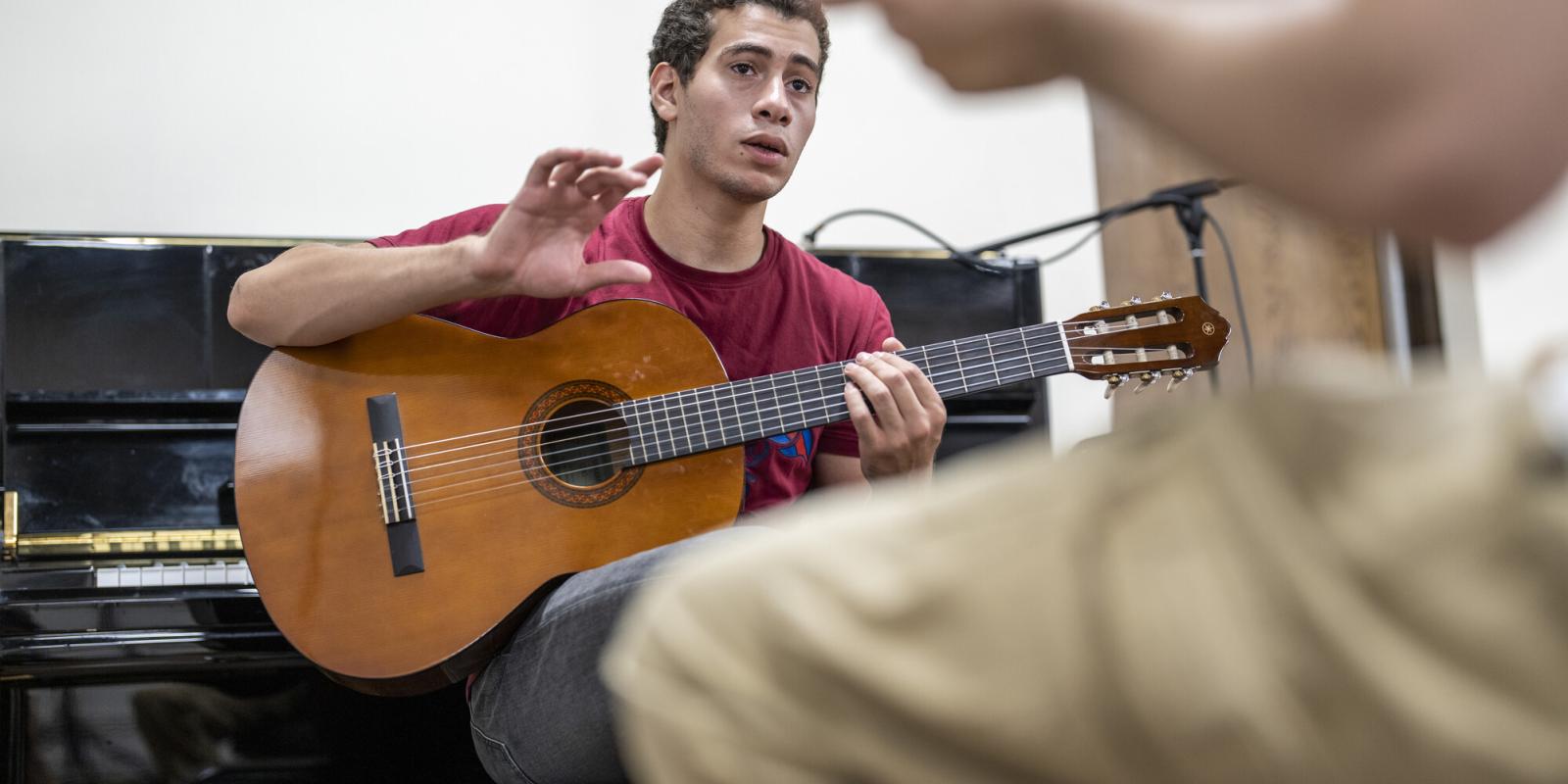 student holding a guitar in studio working with a music professor
