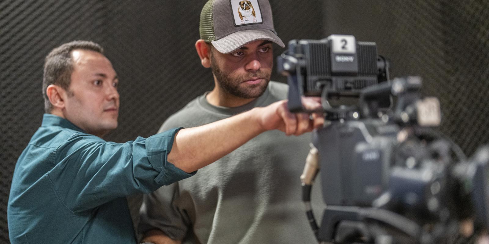 a boy wearing a cap in a studio working with a colleague using a camera