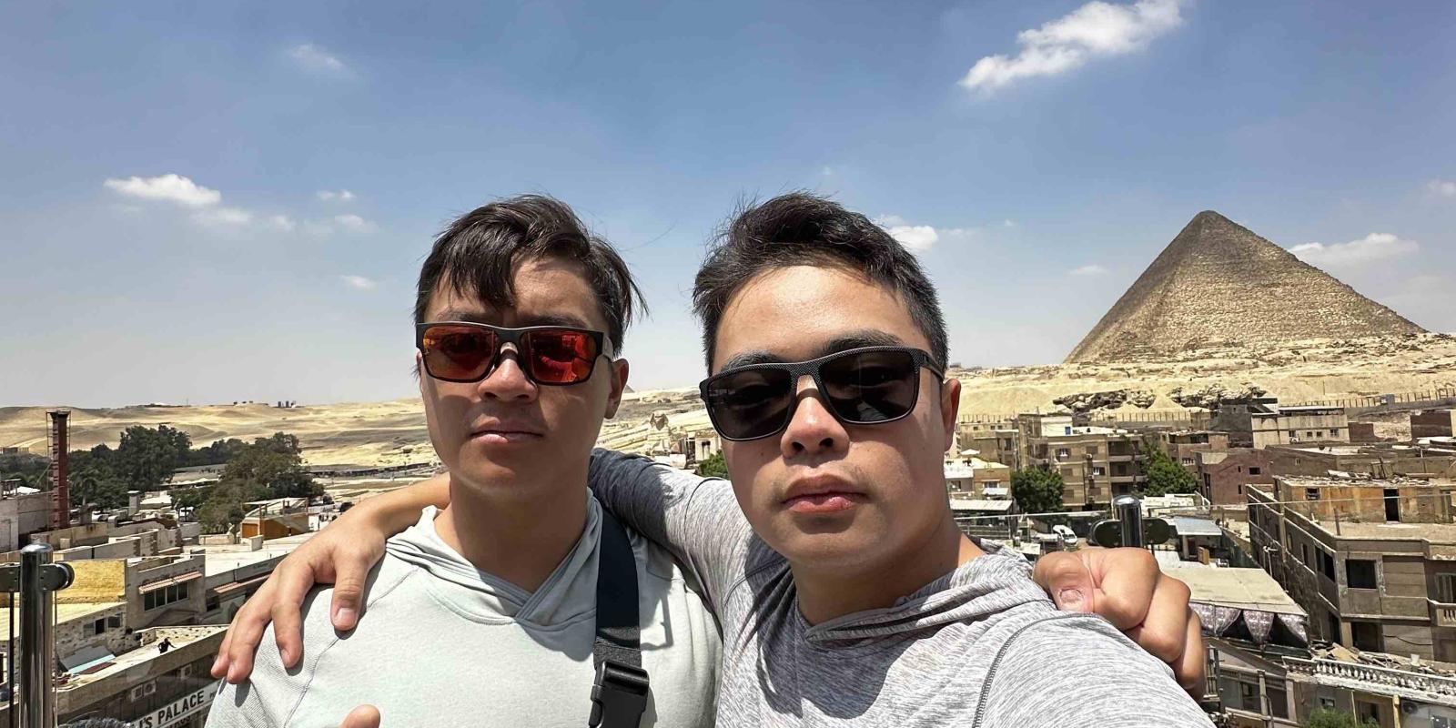two boys wearing sunglasses taking a selfie and smiling at the camera
