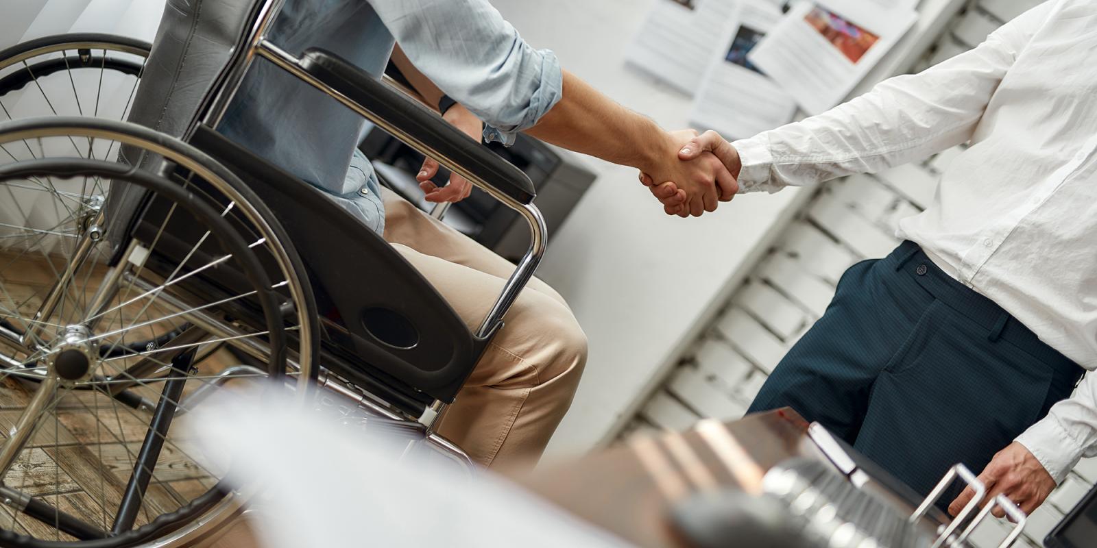 Man in wheelchair shakes hand with man standing up.