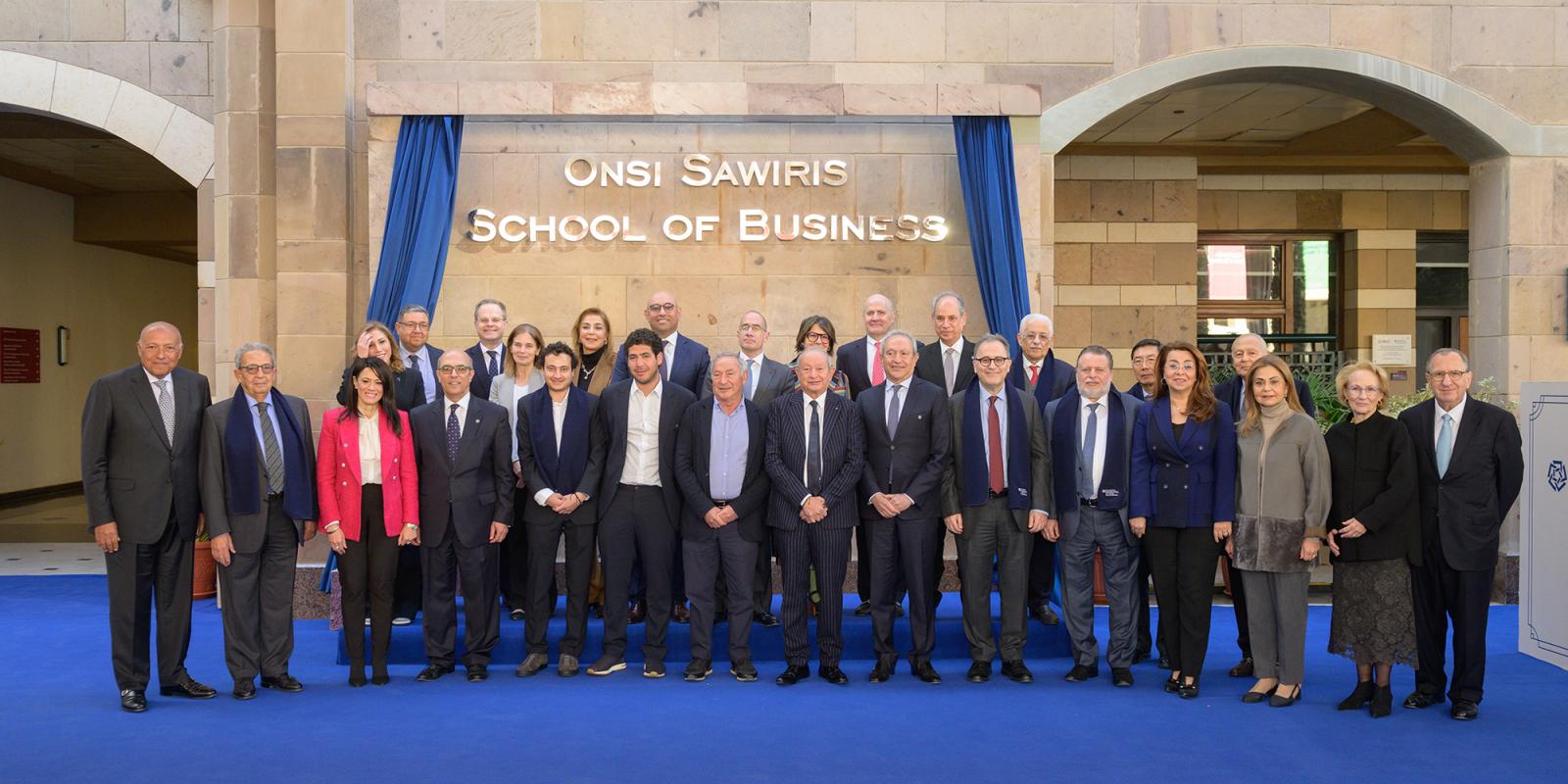 Members of the Sawiris family, senior AUC leadership, ministers, ambassadors and other notable figures standing in front of the Onsi Sawiris School of Business at AUC